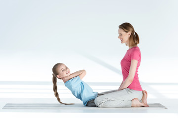 Side view of happy mother training daughter on yoga mat