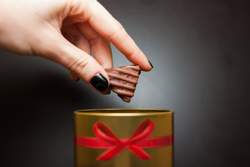 mano che tiene caramella di cioccolato della donna, tirato fuori da una scatola d'oro rotonda con un fiocco rosso su sfondo nero