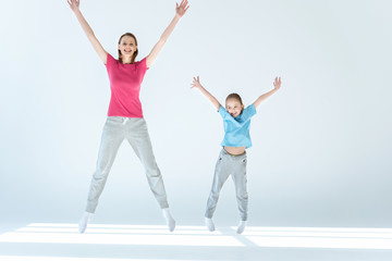 sporty mother and daughter jumping together on white