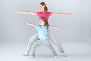 Fototapeta premium Side view of sporty mother and daughter practicing warrior yoga pose together on white