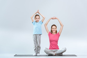 Obraz premium Smiling sporty mother and daughter practicing yoga together on white