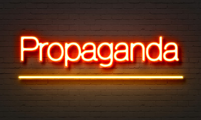 Propaganda neon sign on brick wall background.