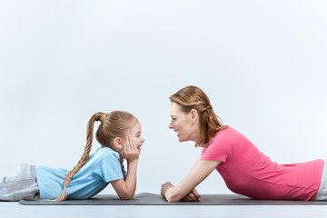 portrait of cheerful mother and daughter looking at each other on white