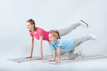 smiling sporty mother and daughter exercising on mats together on white