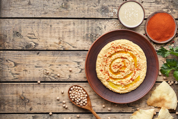 Hummus traditional eastern snack chickpea vegan natural nutrition lunch dip paste with paprika tahini parsley and olive oil in clay plate on rustic flat lay. Healthy dietary fiber protein food