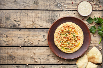 Hummus traditional homemade Israel chickpea vegan natural nutrition dip paste with pita paprika tahini parsley and olive oil in clay plate on rustic flat lay. Healthy dietary fiber protein food