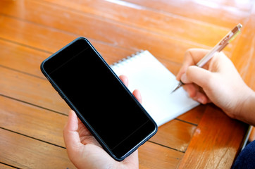 Smart phone in hand with pen handles are writing notebooks.