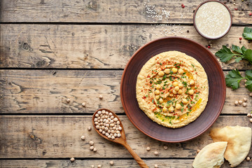 Hummus traditional eastern homemade arabic chickpea dip paste with paprika tahini and olive oil in clay dish on rustic background flat lay. Healthy dietary fiber protein food