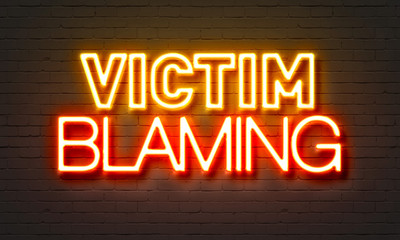 Victim blaming neon sign on brick wall background.