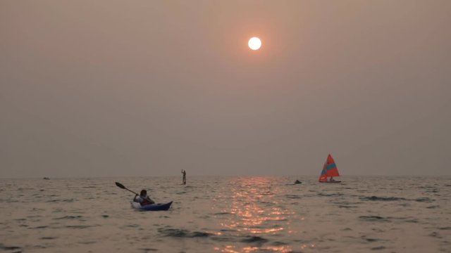 People engaged in different kinds of water sports in the sea at sunset