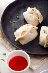 Uzbek dumplings (manti) with sauce and black chopsticks on white background