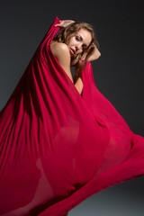 Young beautiful dancer in red dress posing on a dark gray studio background