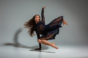 Young beautiful dancer in black dress posing on a dark gray studio background