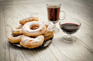 Donuts in powdered sugar, a mug of tea and currant jam on a wooden background