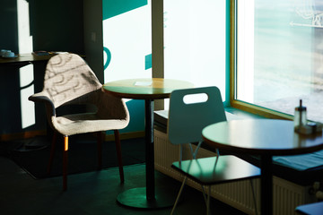 Image of empty seating area in cafe, tables with chairs standing by window in bright sunlight