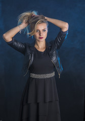 Portrait of attractive blonde woman in black skirt and leather jacket looking at camera in studio shot, on dark background