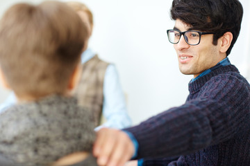Portrait of young man wearing glasses patting his friend on shoulder congratulating him in group meeting