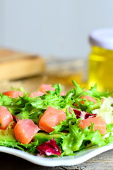 Fresh salad mix with smoked salmon and avocado and  dressing with olive oil and lemon juice. Healthy and quick salad on a plate. Vertical photo. Closeup