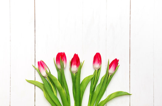 Bouquet of pink tulips on a white rustic wooden background with a nd for text at the top. View from above.