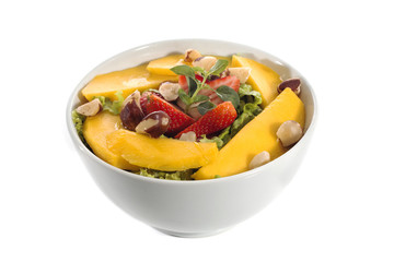 A healthy fresh salad of green lettuce with nuts, mango, strawberry, tomatoes in a white bowl isolated over white background.