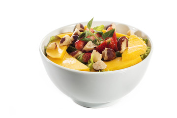 A healthy fresh salad of green lettuce with nuts, mango, strawberry, tomatoes in a white bowl isolated over white background.