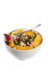 A healthy fresh salad of green lettuce with nuts, mango, strawberry, tomatoes in a white bowl isolated over white background.