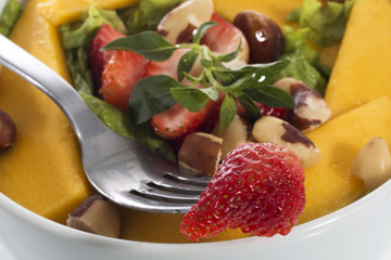 A healthy fresh salad of green lettuce with nuts, mango, strawberry, tomatoes in a white bowl isolated over white background.