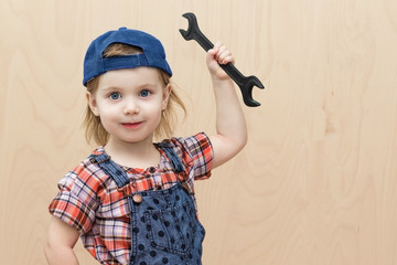 Cute little girl look like a worker in blue cap, checkered shirt and denim overalls. With a wrench...