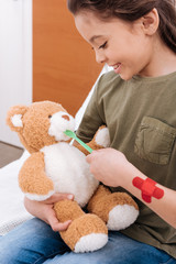 side view of smiling girl playing doctor and patient with teddy bear