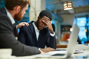 Overworked businessman showing tiredness, his colleague reassuring him - obrazy, fototapety, plakaty