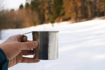 Man hand hold steel metal cup of tea with forest background. Relax time in spring sunny day. Outdoor tourism concept. Health and fresh air walking.