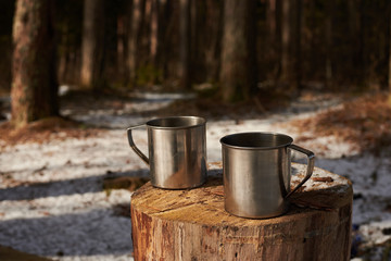 Fototapeta premium Two cups of tea on the stump in forest. Time for relax break. Sunny spring day. Walking out of town concept. Traveler camping.