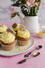 Delicious cupcakes with yellow cream and white flowers on pink background (close-up)