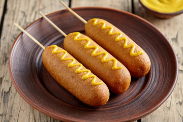 Corn dog traditional American corndog street junk food deep fried hotdog meat sausage with mustard snack treat coated in layer of cornmeal batter on stick unhealthy eating on rustic wooden desk.