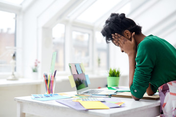 Young woman holding her head in hands over workplace