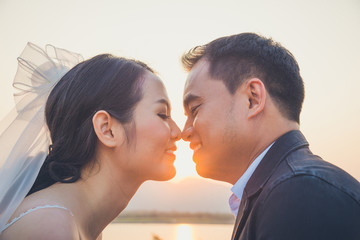 Asian bride and groom kissing at sunset