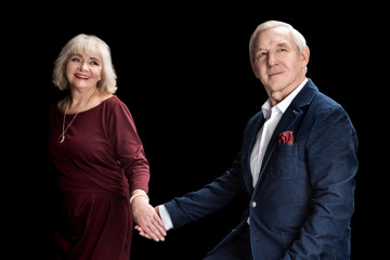 Happy senior couple holding hands and looking away on black