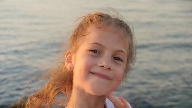 beautiful little girl on a background of sea sunset smiles showing her teeth
