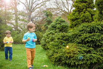 Kids on Easter egg hunt in blooming spring garden. Children searching for colorful eggs in flower meadow. Toddler boy and his brother friend kid  play outdoors