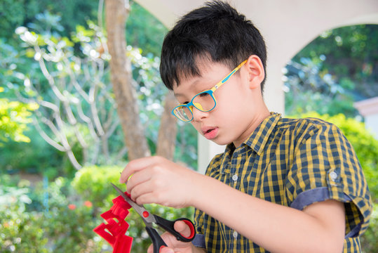 Young Asian Boy Cutting Paper By Scissors