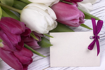 Purple and white tulips with white paper on a white wooden background with card for text. Womans Day. 8 March. Mother's Day.