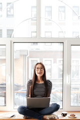 Vertical image of Asian woman on windowsill with laptop