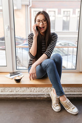 Fototapeta premium Vertical image of Asian woman talking phone on windowsill