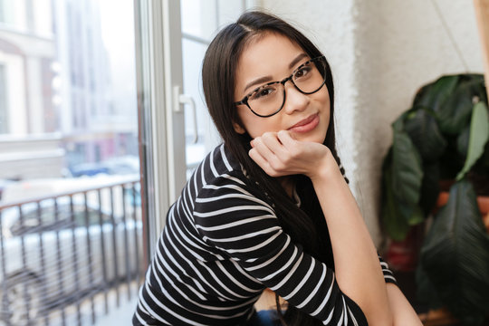 Side view of Young Asian woman sitting on windowsill