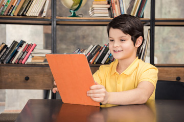 Smiling schoolboy sitting at table and using digital tablet