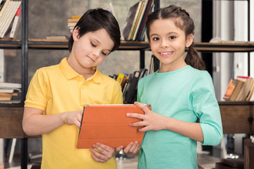 Cute smiling schoolchildren using digital tablet together