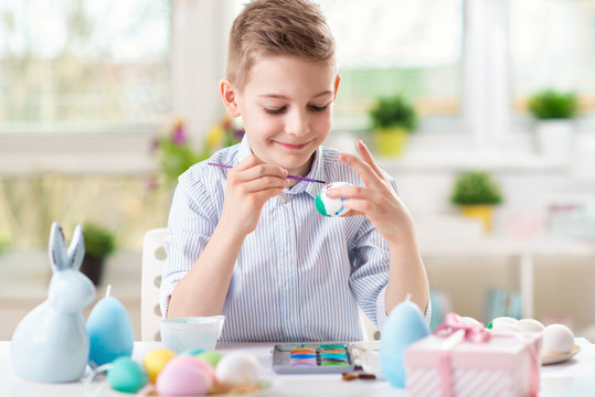 Happy child boy having fun during painting eggs for Easter in spring at home