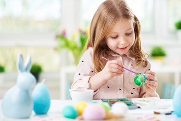 Happy pretty child girl having fun during painting eggs for Easter in spring at home