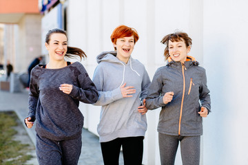 Front view of the group of three athletic women jogging outside in sunny morning.