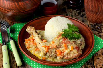 Rabbit leg with cream sauce with carrots and onions and rice side dish on a clay plate